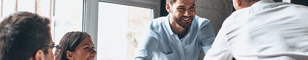 Two smiling men looking at each other in an office setting, with a smiling man and woman alongside.